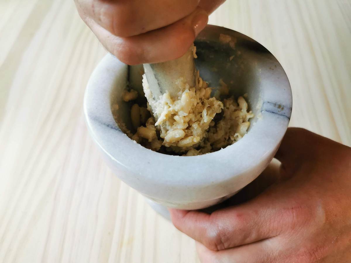 garlic and pine nuts being crushed using a pestle and mortar