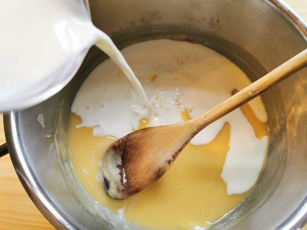 Milk being poured into saucepan with flour and butter roux.