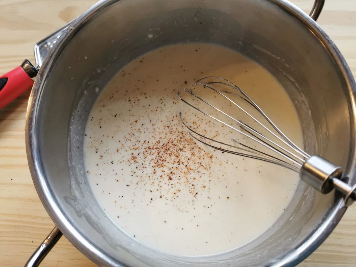 Ready béchamel in saucepan with grated nutmeg on top.