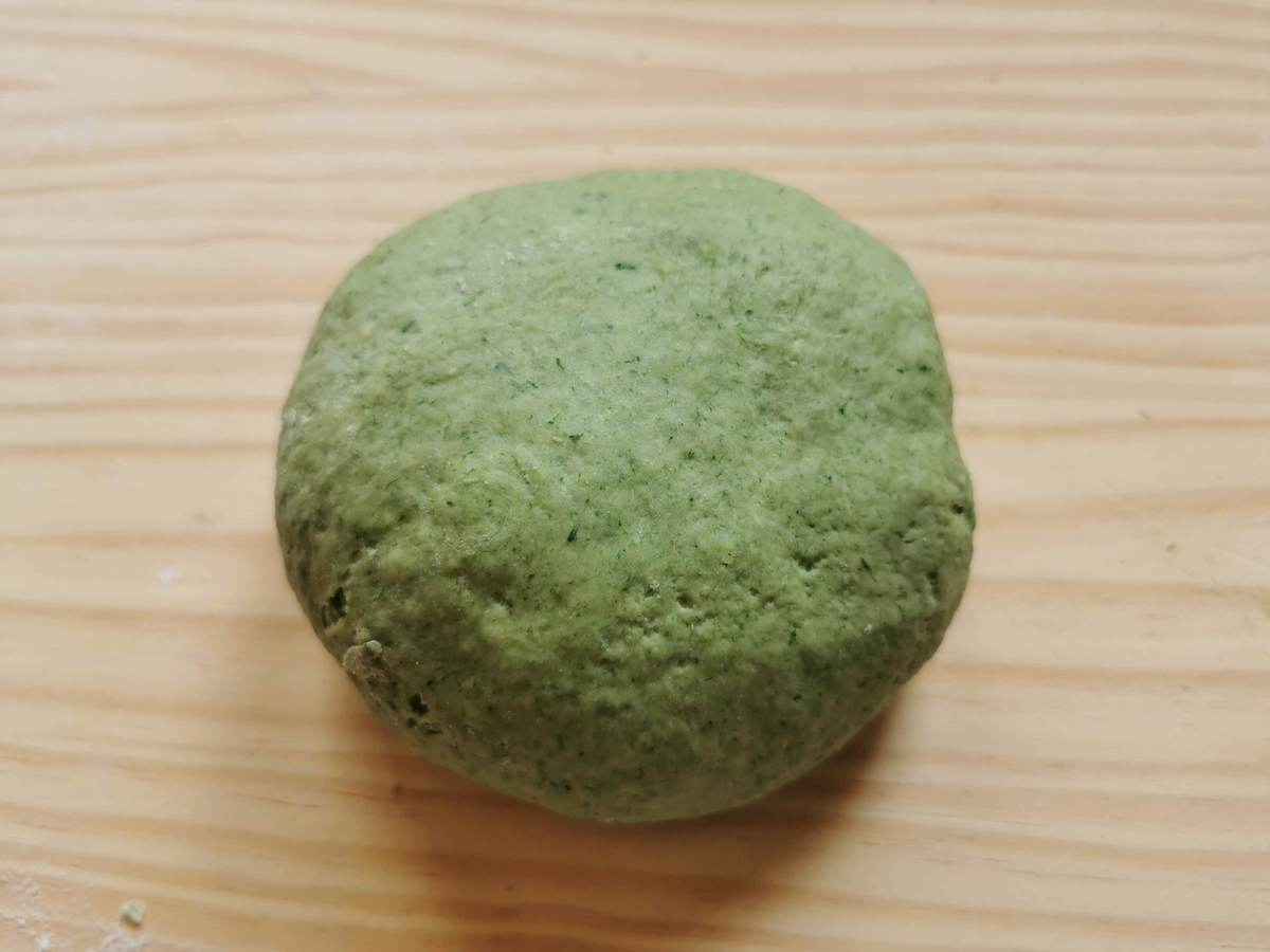 A ball of ready green colored pasta dough on wood work surface.