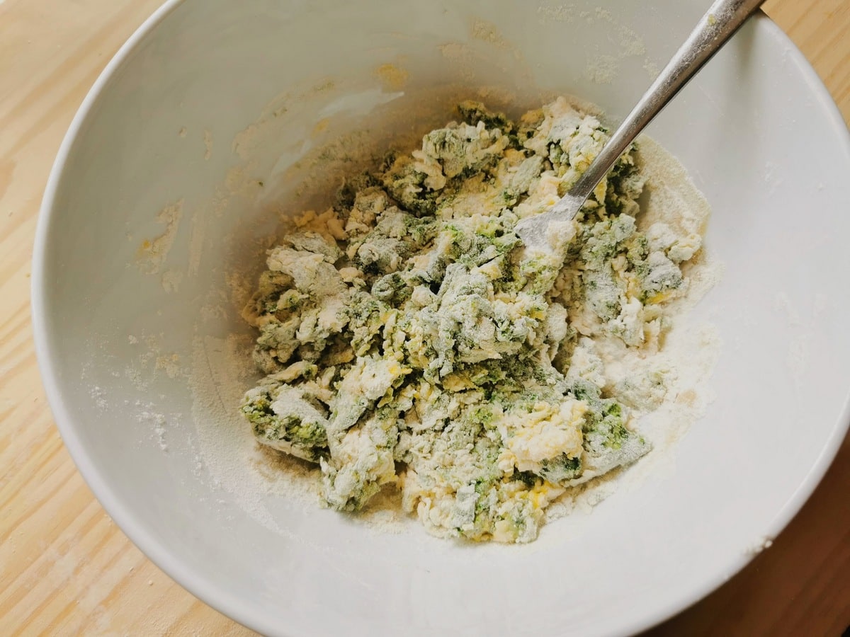 Flour, eggs, spinach, salt and olive oil mixed together in a bowl with a fork.