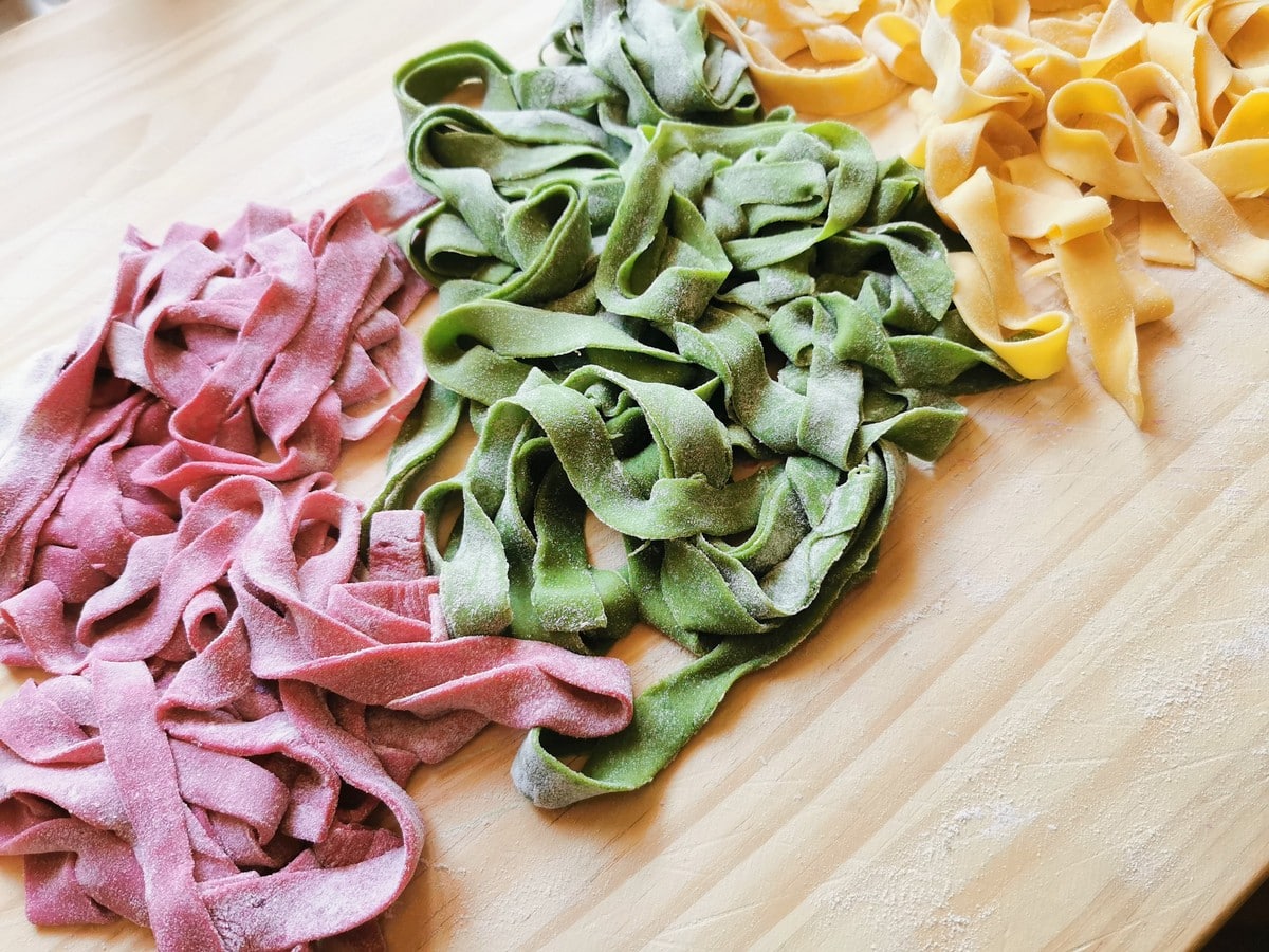 Red, green and natural pasta ribbons on wood work surface.