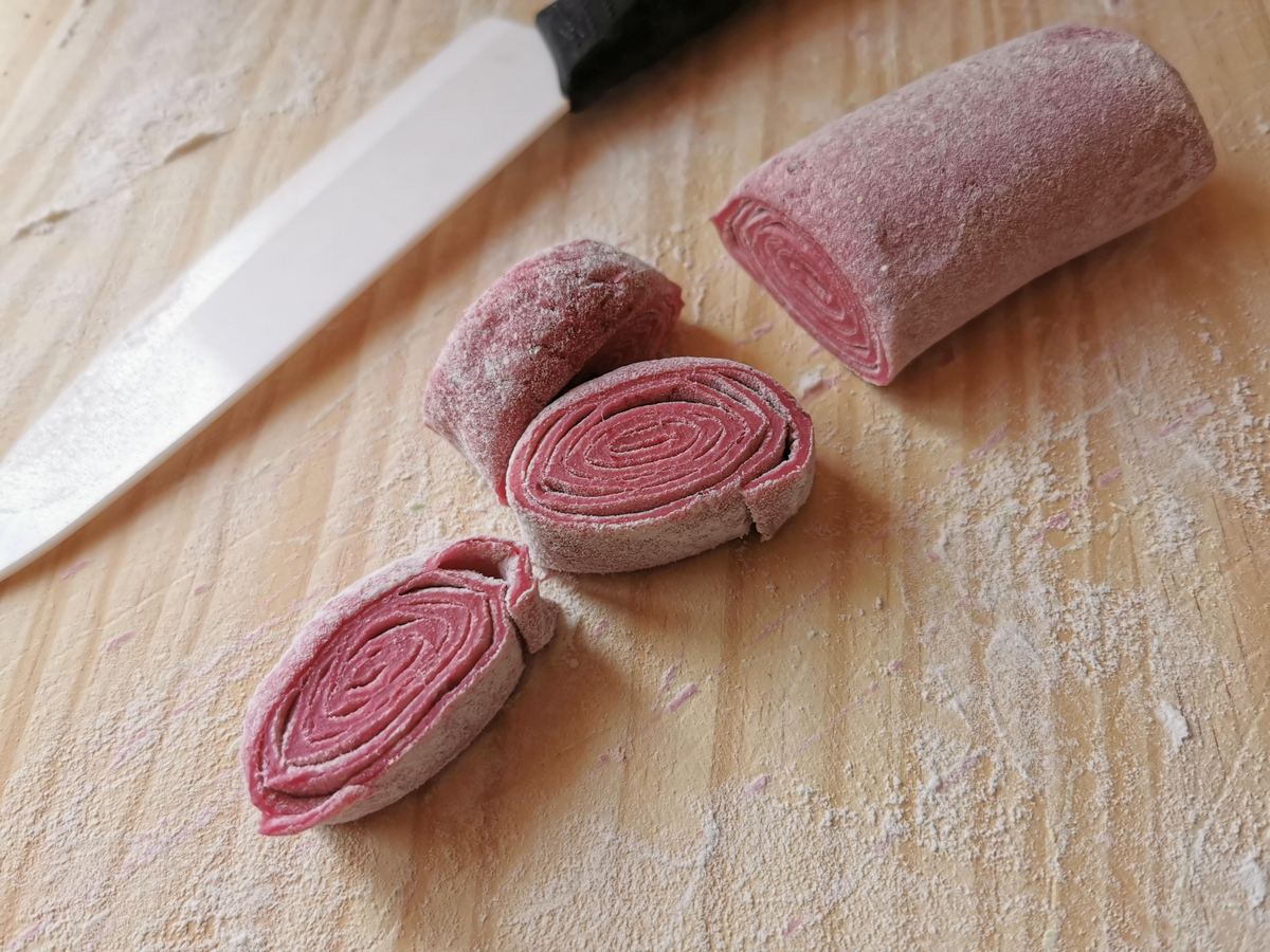 Red colored pasta dough sheet rolled up and cut into ribbons.