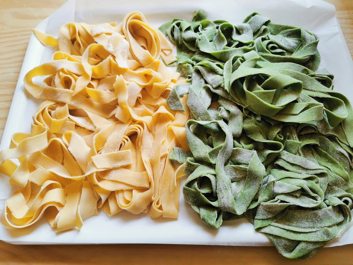 Green and plain homemade egg pasta on tray.