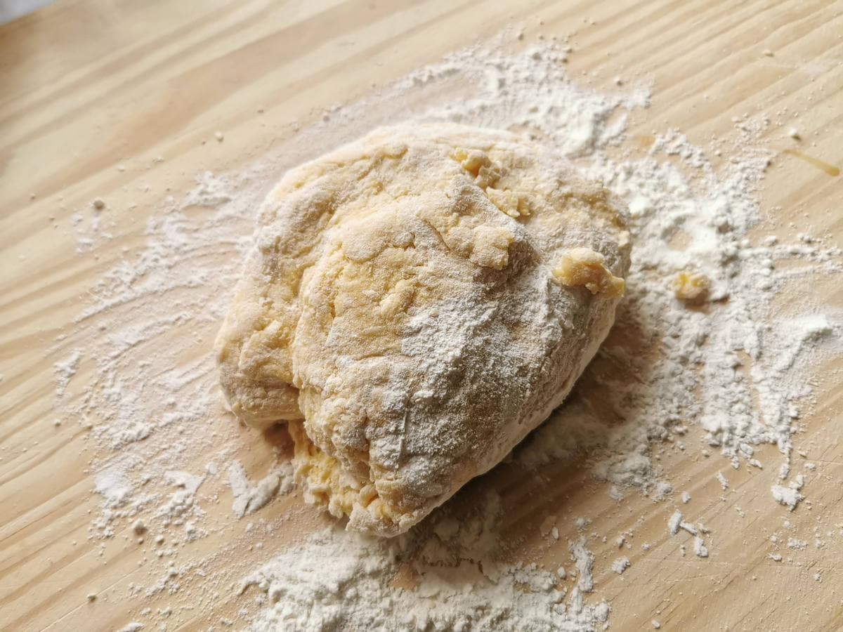 Ball of fresh egg pasta dough on flour dusted wood pastry board.