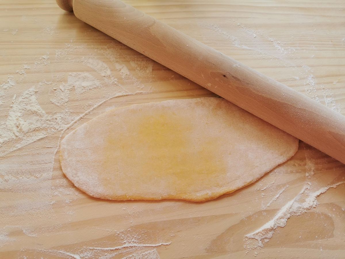 Rolling pin and homemade egg pasta dough rolled out on floured wood work surface.