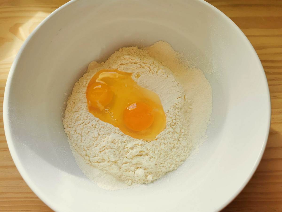 Sifted flour with 2 eggs in white bowl.