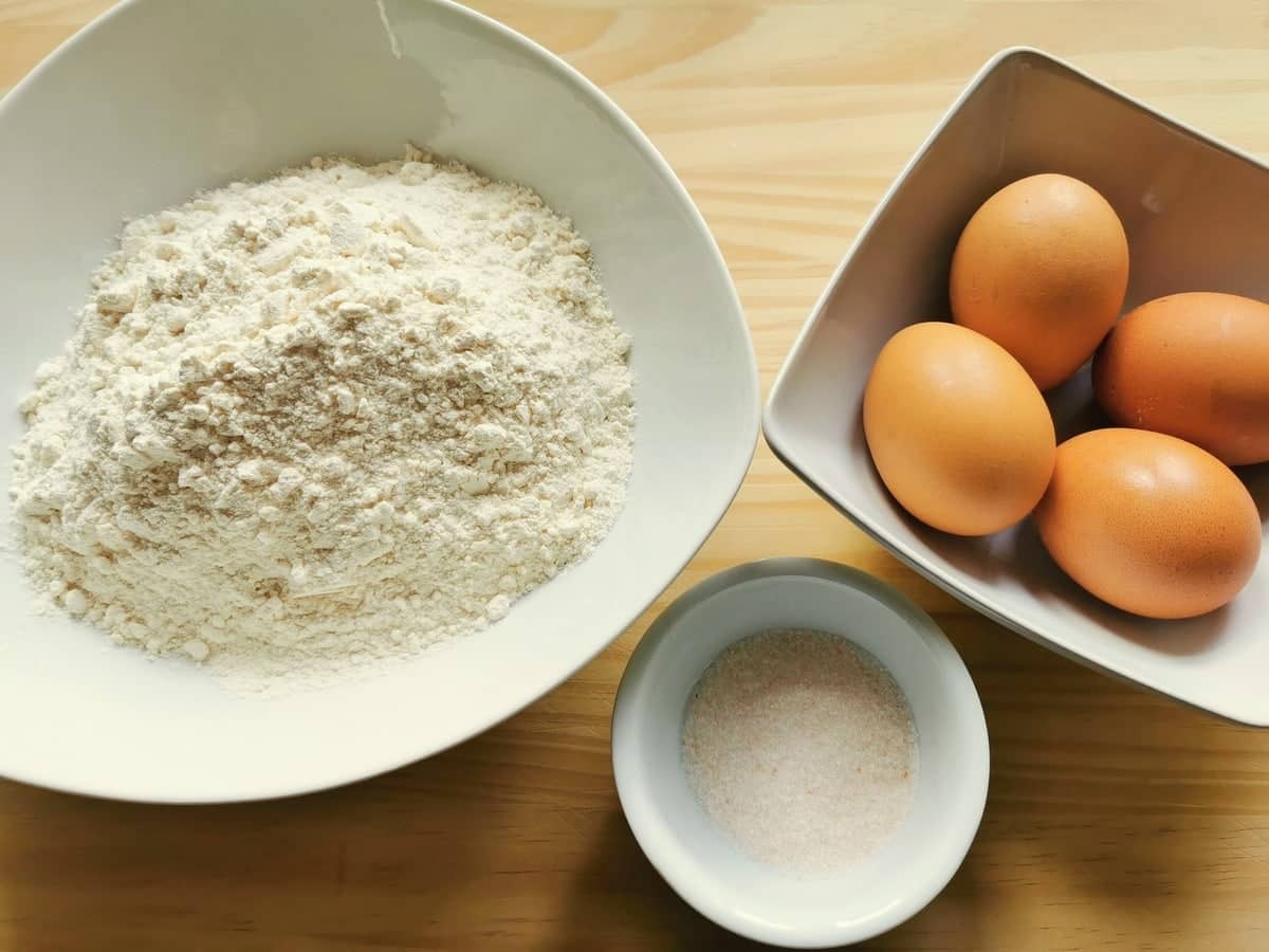 Flour, 4 eggs and salt in separate white bowls.