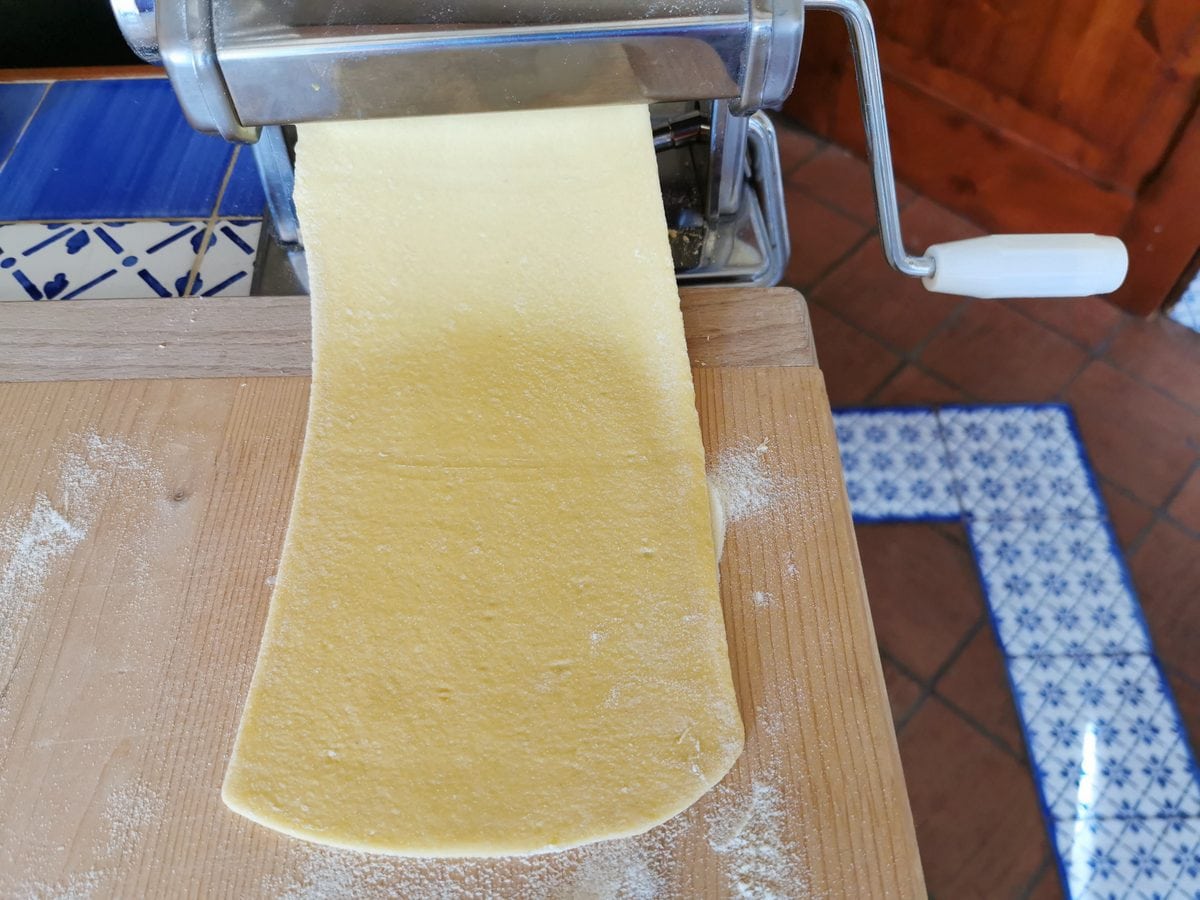 Sheet of pasta dough passing through hand operated pasta machine.