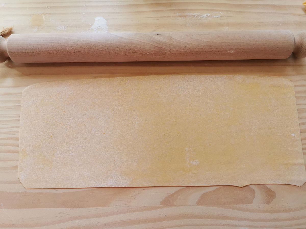 large rectangular pasta dough sheet on wood pastry board with rolling pin.