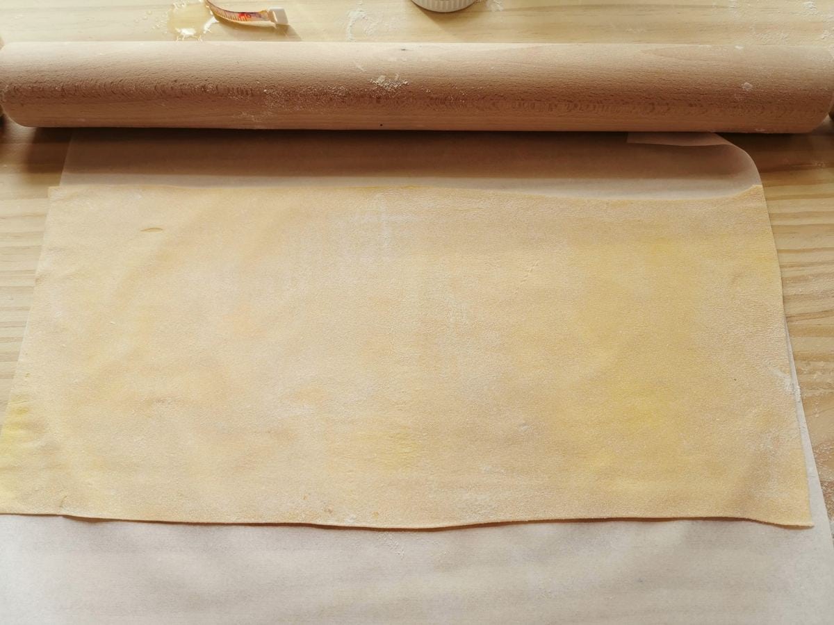 Large rectangular sheet of fresh pasta on wood worksurface with rolling pin.