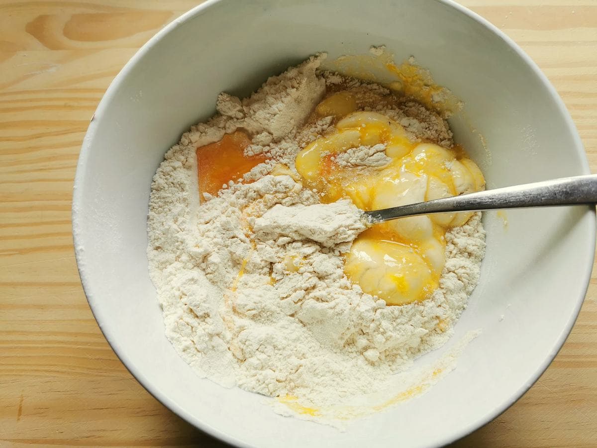 Flour and eggs being mixed together in a white bowl using a fork