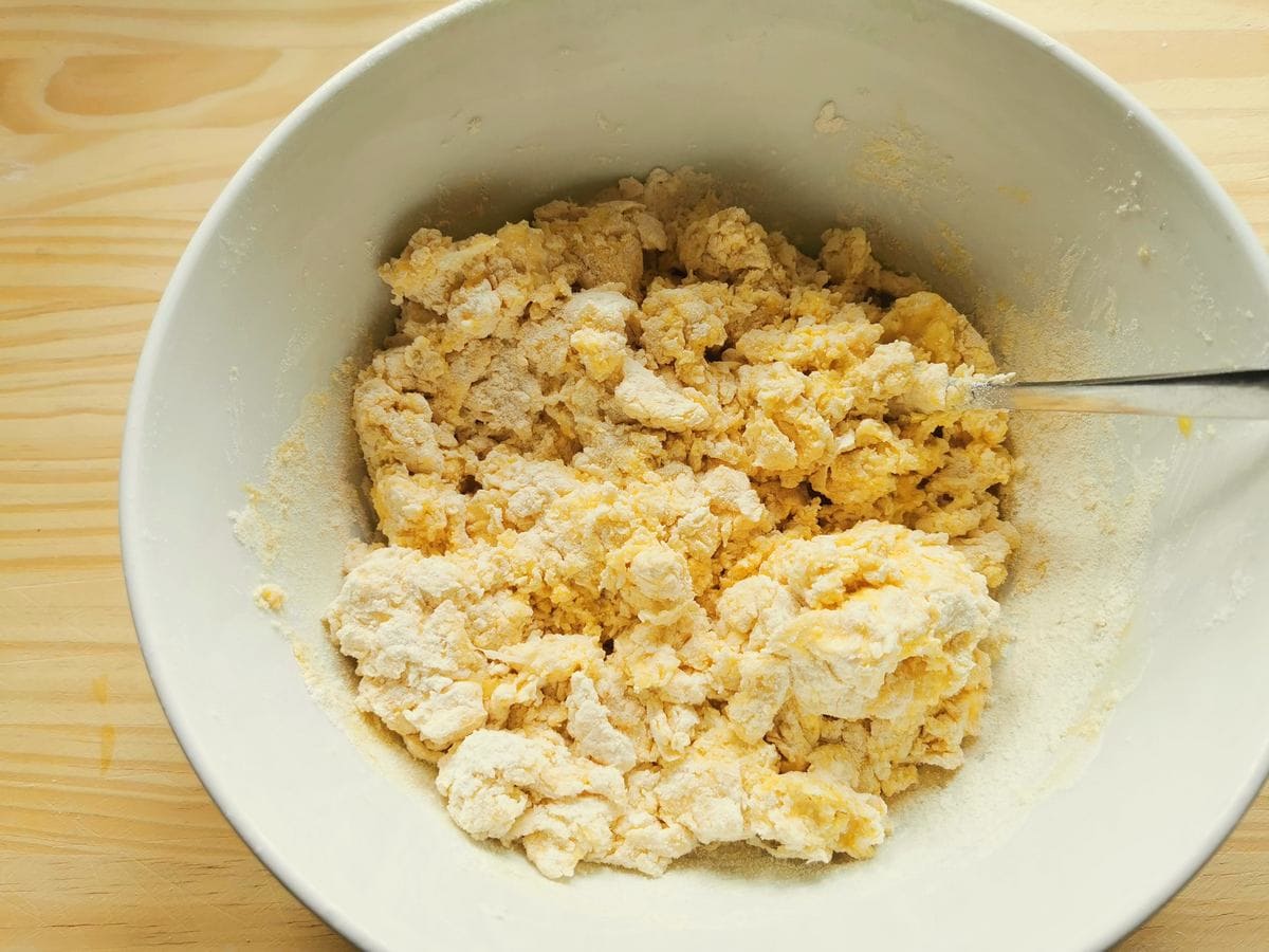 Flour and eggs mixed to form a dough in a white bowl.