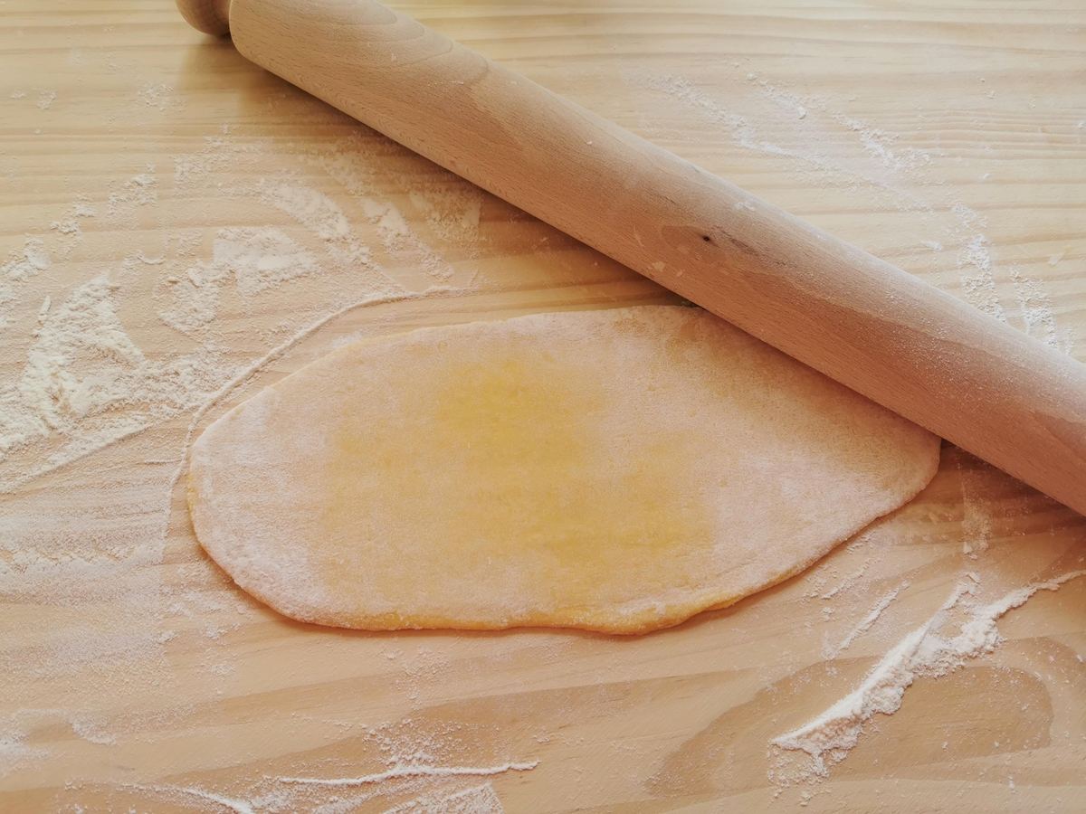 Flattened piece of pasta dough on floured wood work surface.