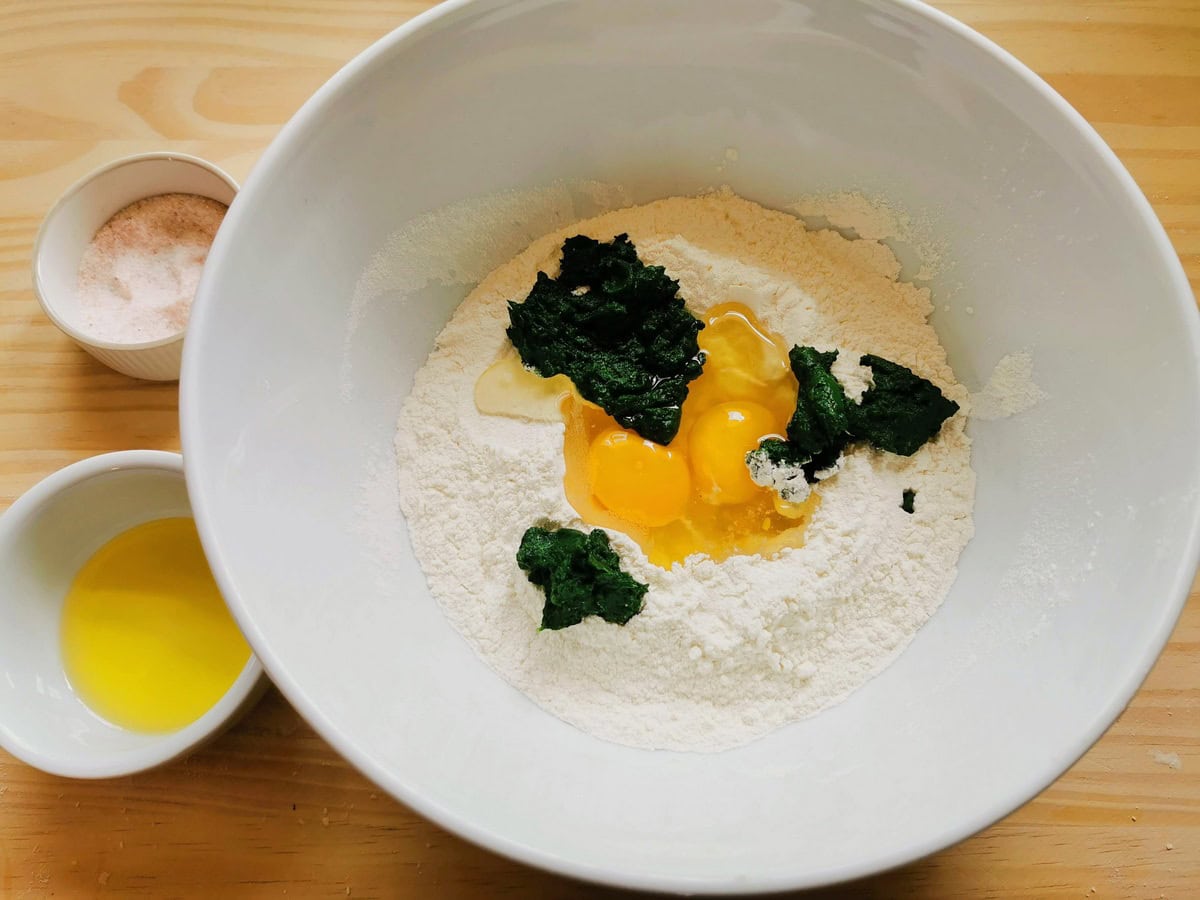Flour, eggs and cooked spinach in white bowl.