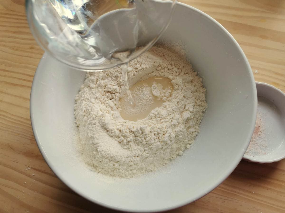 Water being poured into flour in a white bowl.