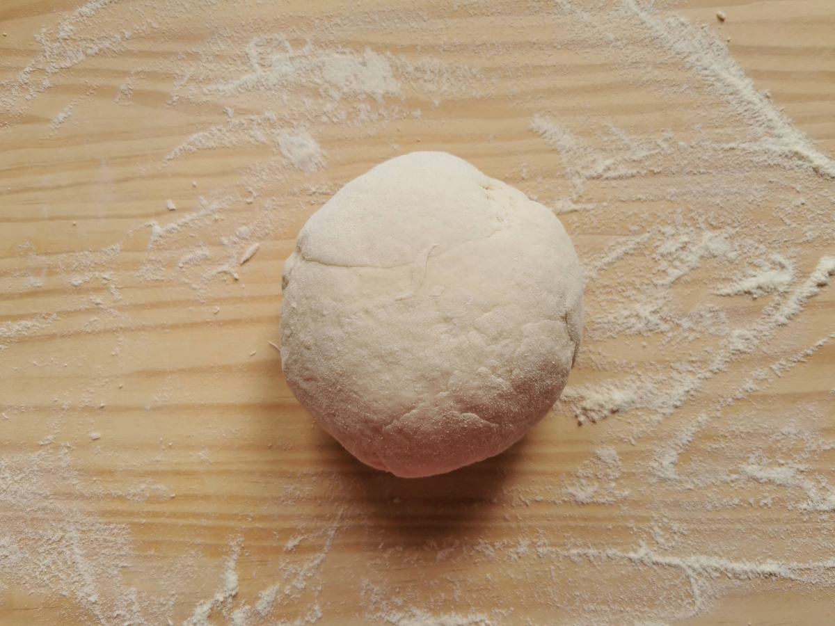 Ball of ready kneaded strangozzi pasta dough on wood worktop dusted with flour.
