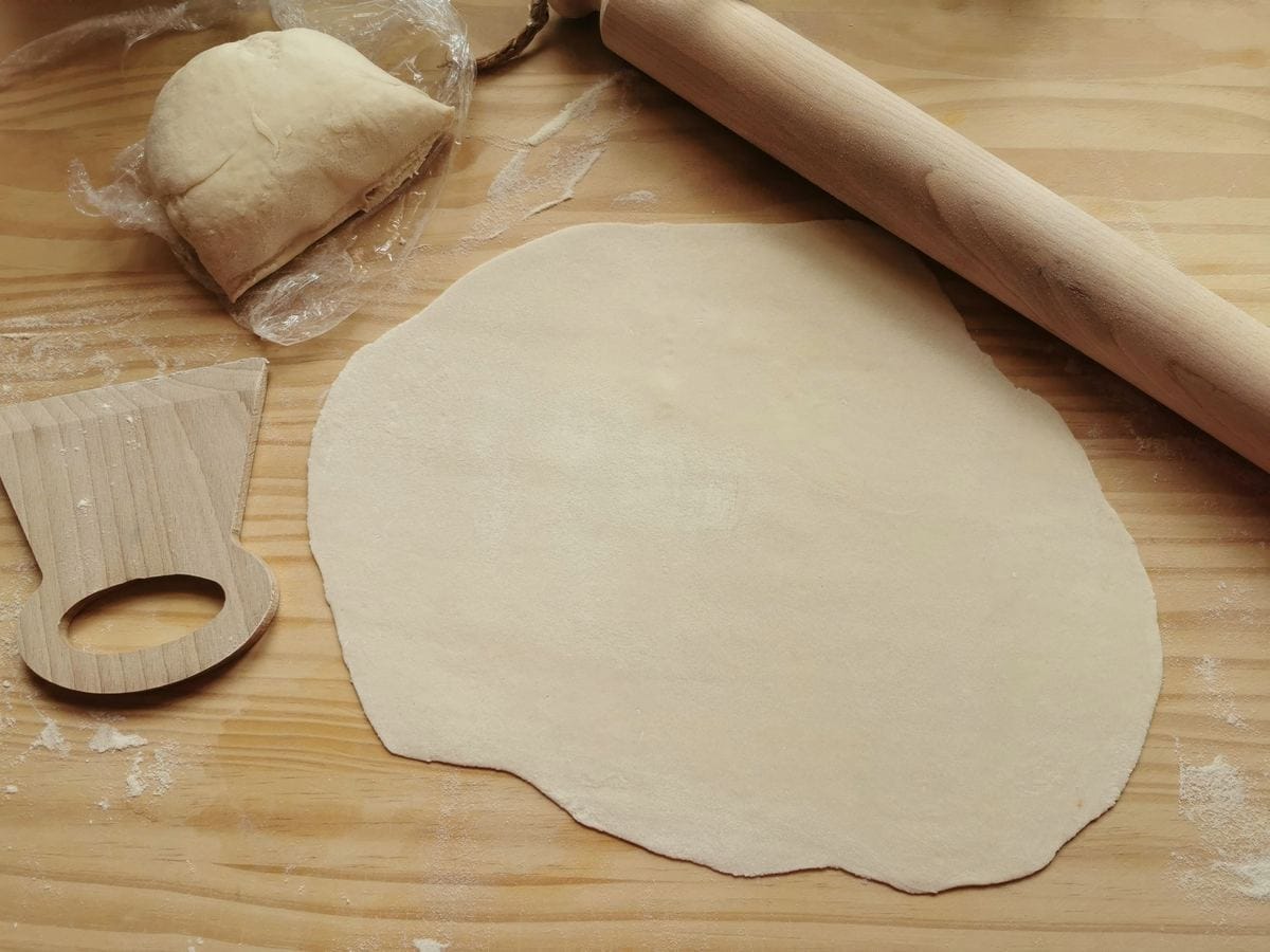 Rolled out sheet of strangozzi pasta dough on wood worktop with rolling pin.