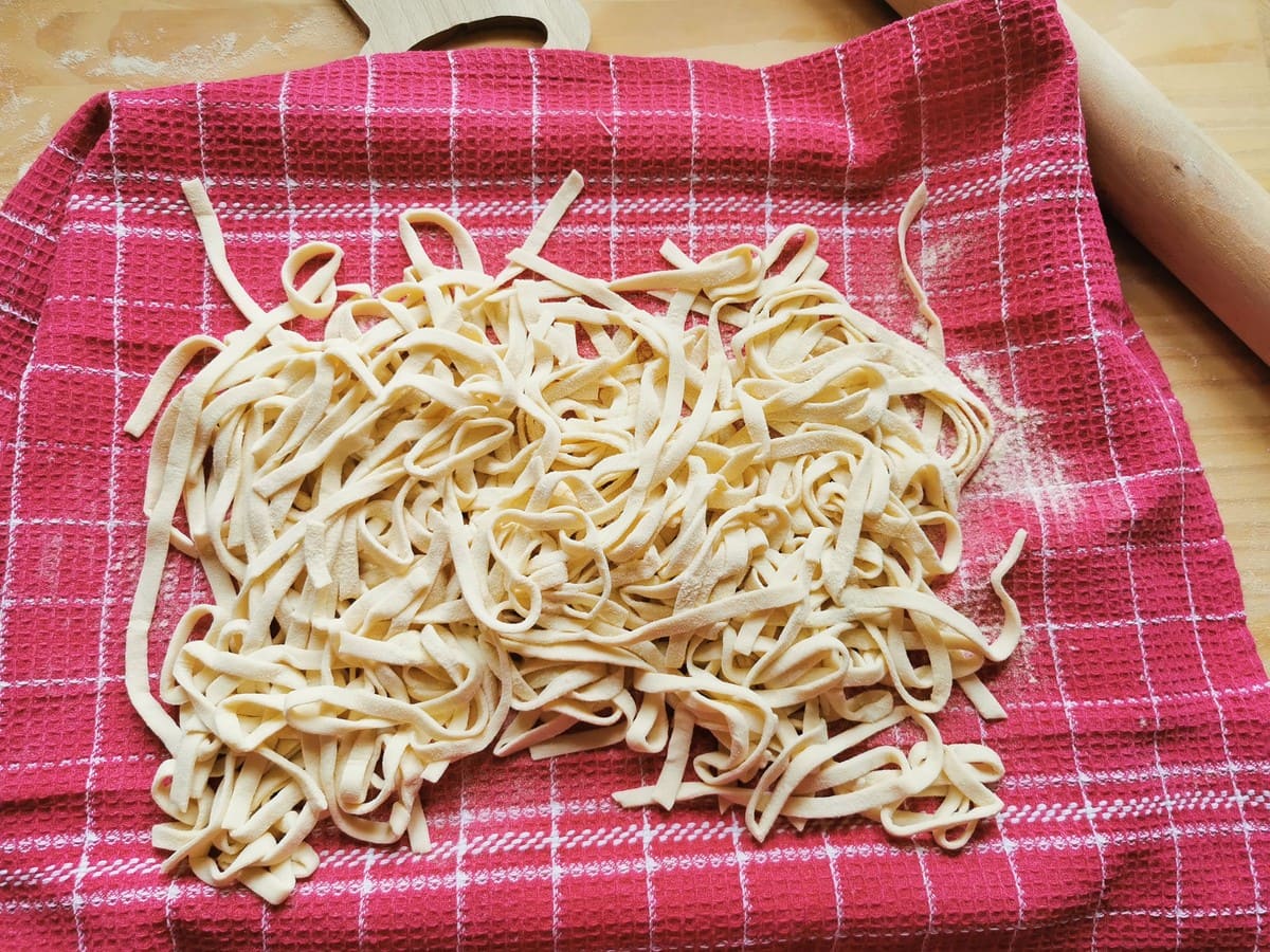 Ready strangozzi pasta on flour dusted red tea towel.