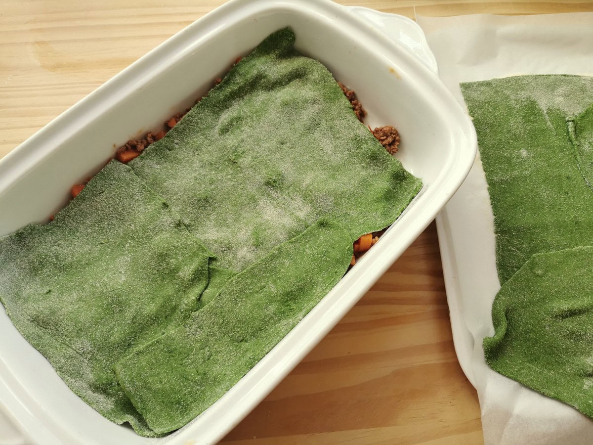 Bolognese sauce in a white rectangular oven dish with green lasagne sheets on top of it.