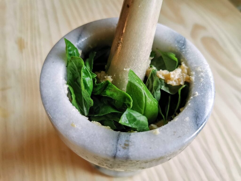 basil leaves in mortar with garlic and pine nuts