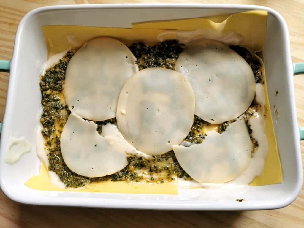 Provola cheese slices on top of pasta sheets, béchamel and pesto in oven dish.