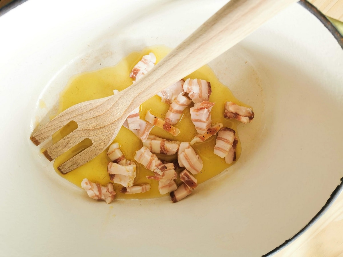 Pieces of pancetta cooking in olive oil in Dutch oven.