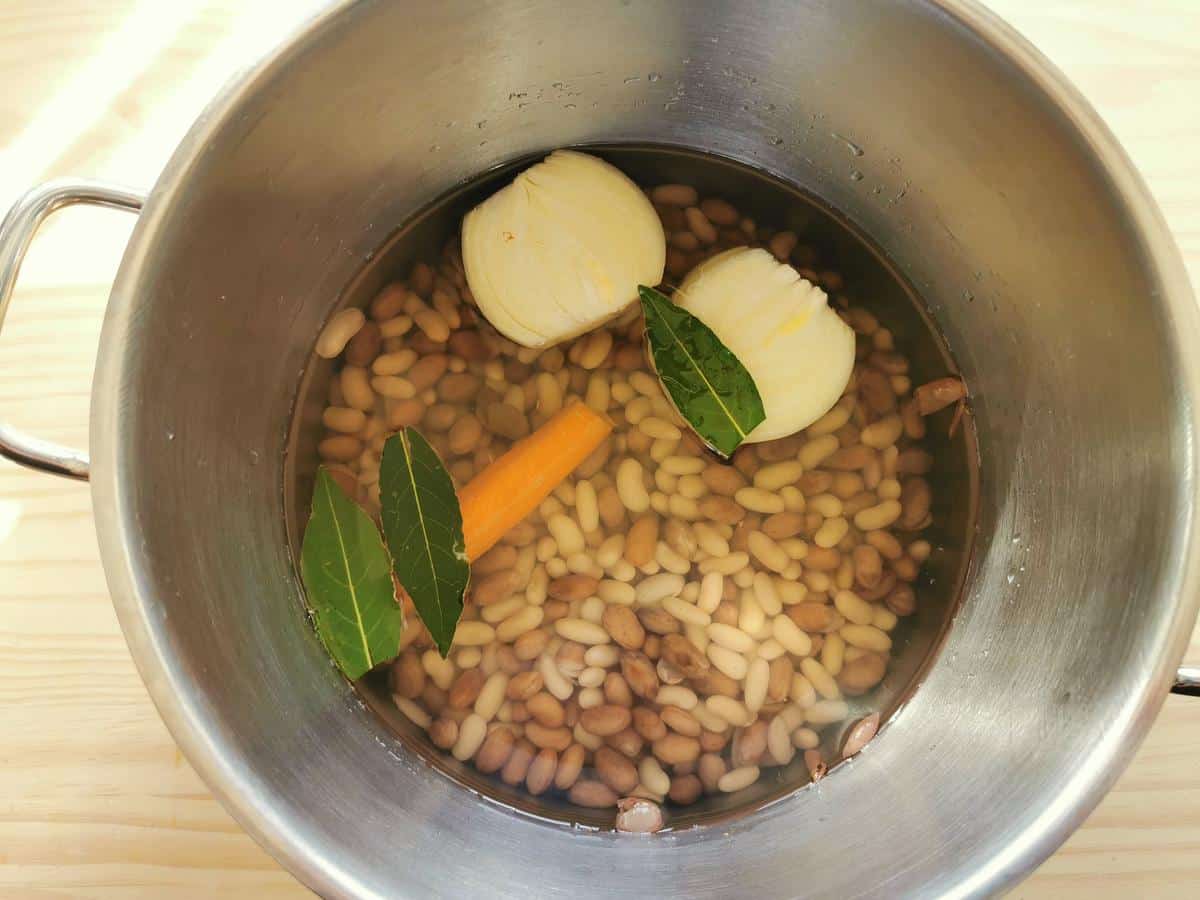 Borlotti and cannellini beans in pot of water with a peeled onion and carrot and 3 bay leaves.