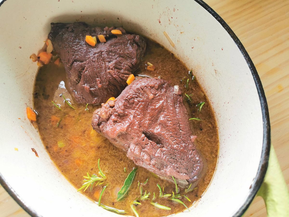 Beef cheeks cooking in red wine, broth and vegetables in Dutch oven.