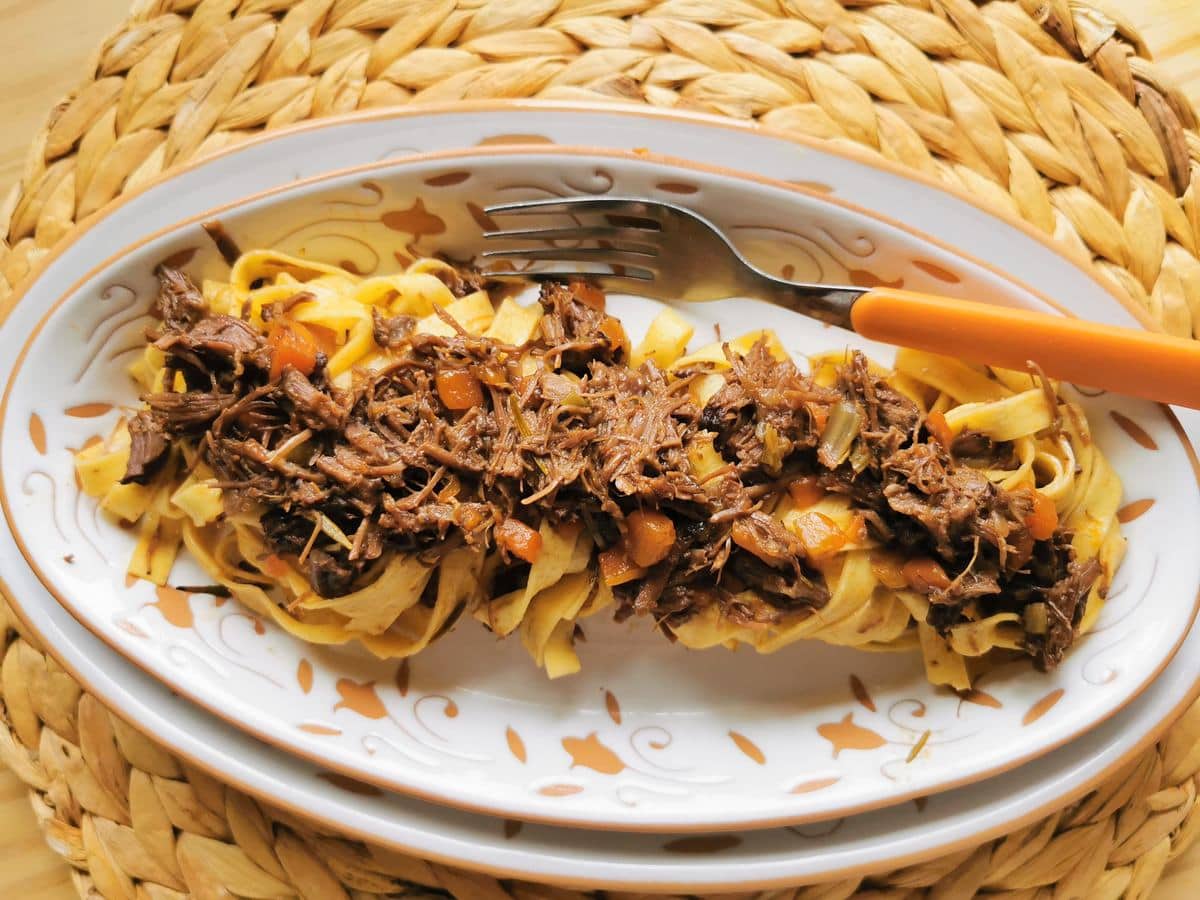 Slow cooked Italian beef cheek ragu with tagliatelle in oval plate.