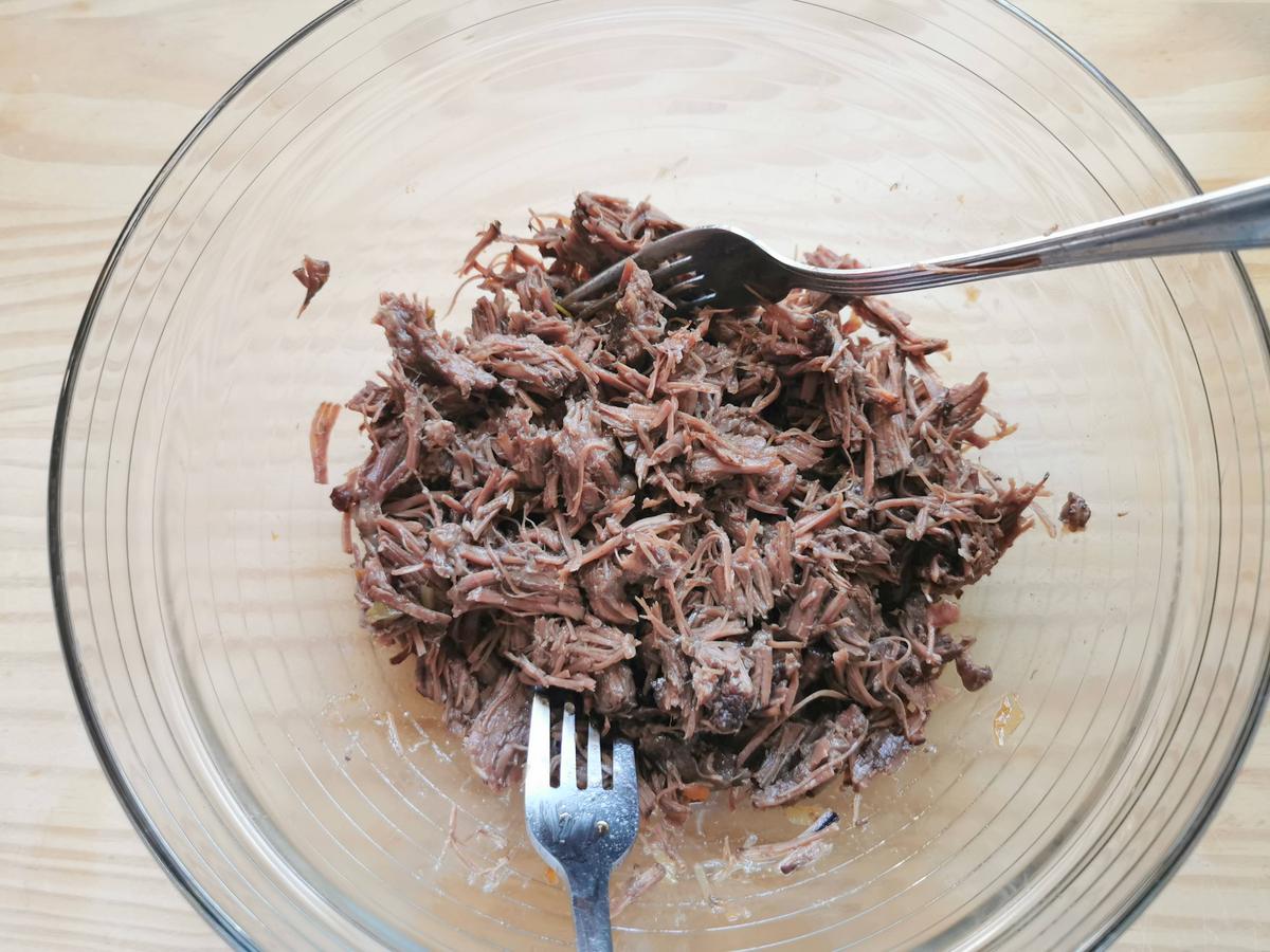 Cooked and shredded beef cheek in a glass bowl.