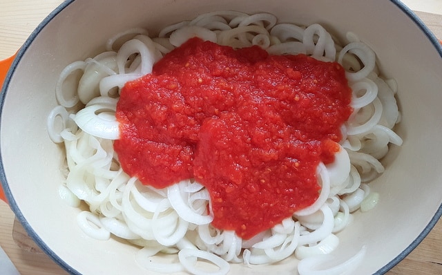 tomato pulp and sliced white onions in Dutch oven