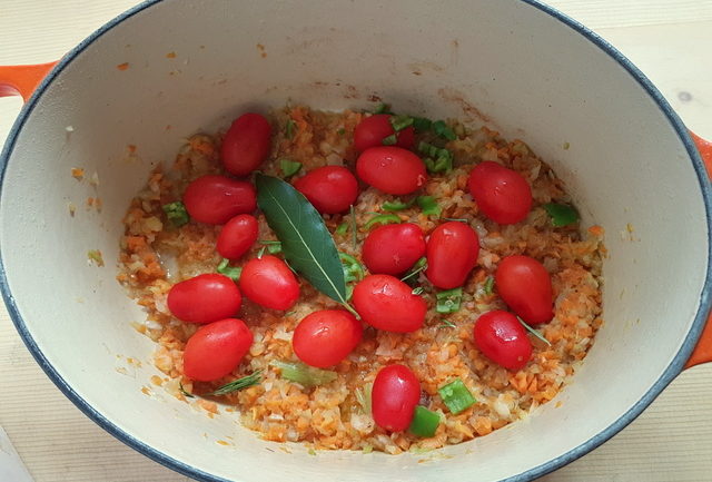 chopped onion, carrots, celery, chili pepper in dutch oven with cherry tomatoes and bay leaf