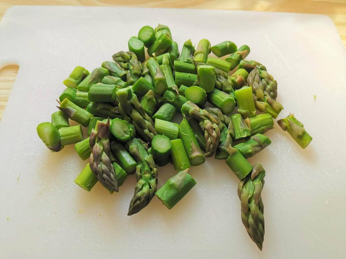 boiled asparagus cut into pieces on white cutting board