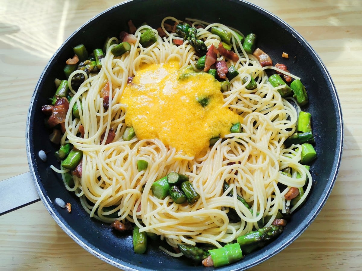 beaten eggs and grated cheese added to spaghetti, asparagus and guanciale in skillet