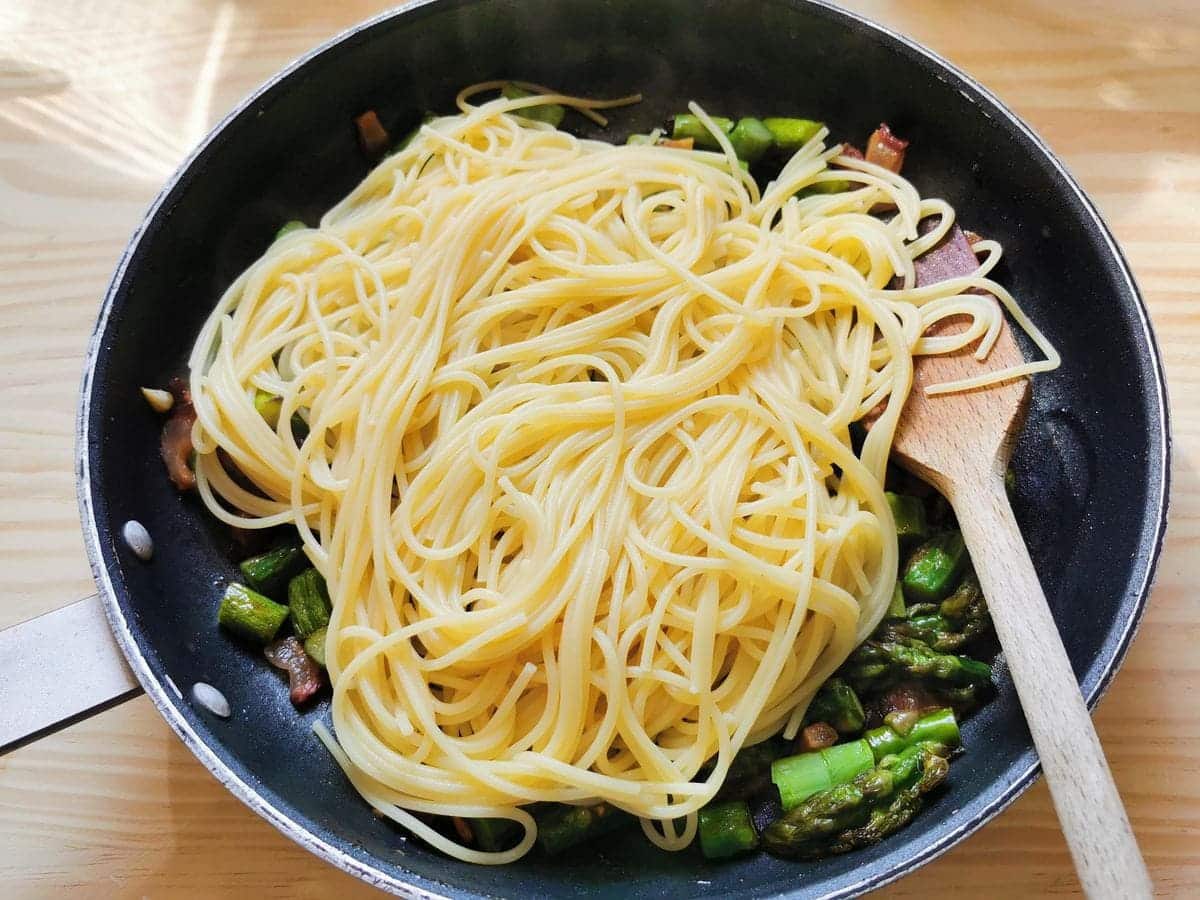 Cooked spaghetti in skillet with asparagus and guanciale.