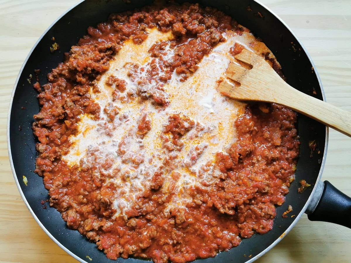 Fresh cream added to beef ragu in frying pan.