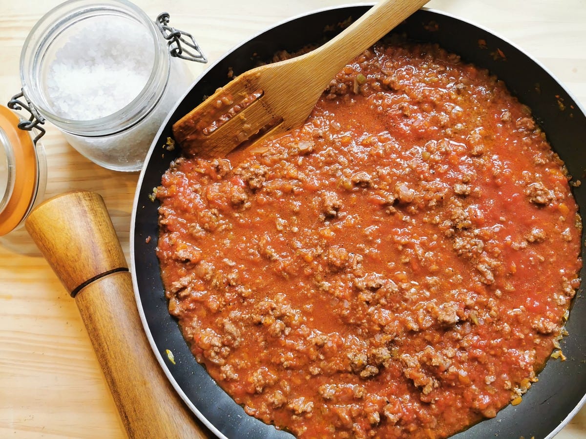 Ground beef ragu in frying pan next to pepper mill and jar with salt.