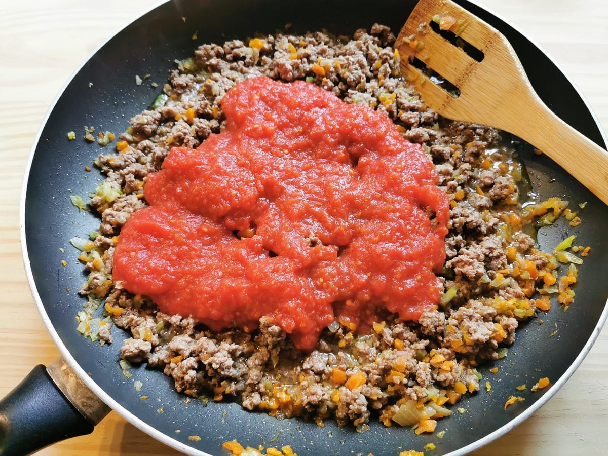 Tomato passata in frying pan with ground beef and vegetables.