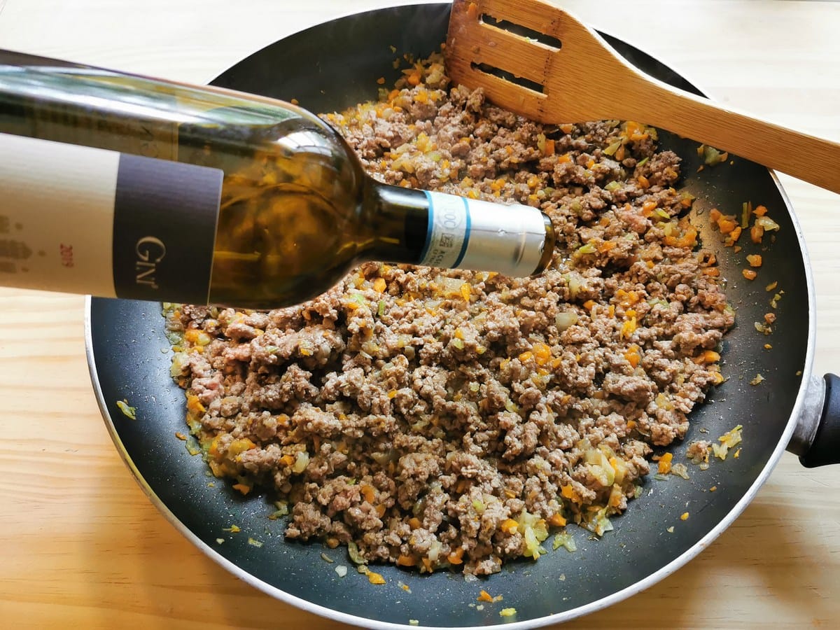 Wine being added to beef and vegetables in frying pan.