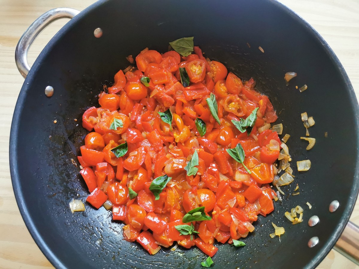 Torn fresh basil leaves added to large skillet with tomato and sweet pepper sauce in it.