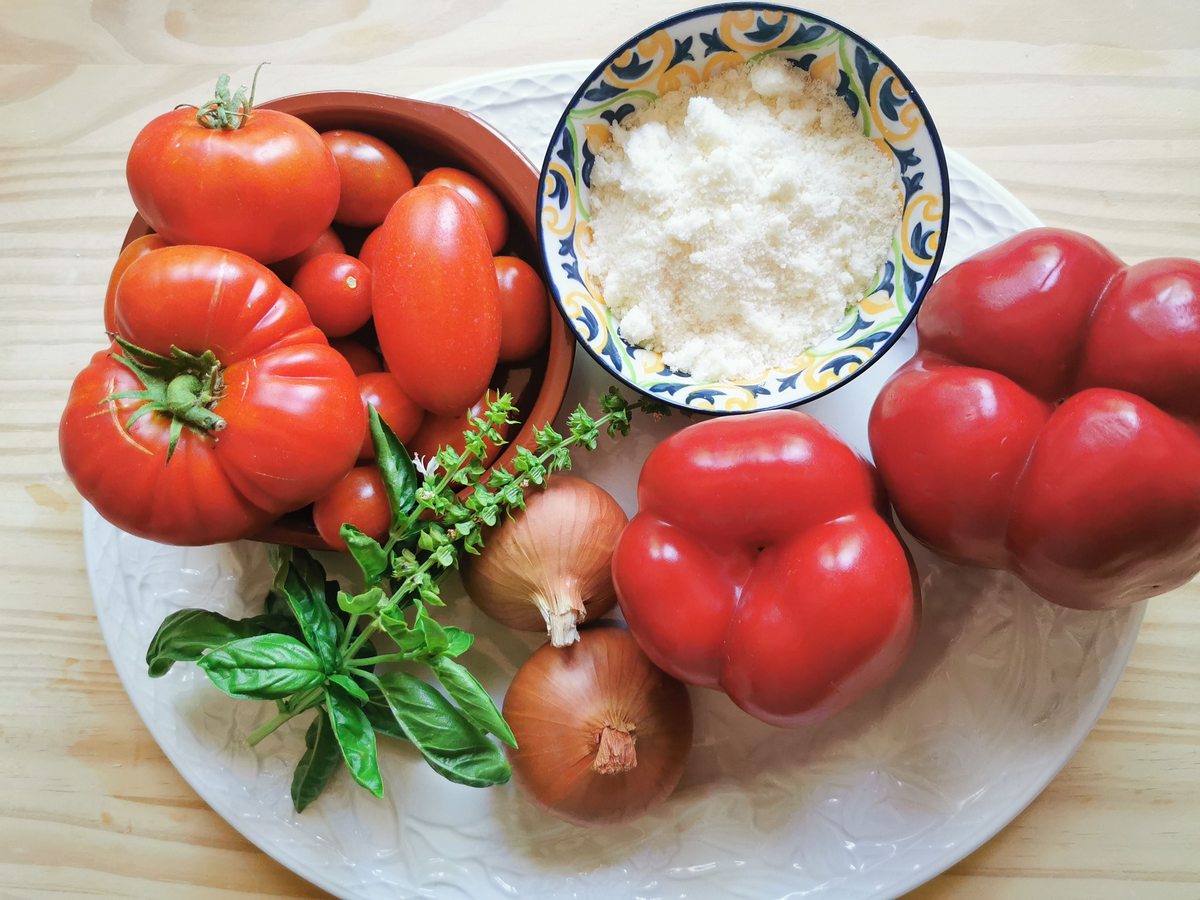 Ingredients for tagliatelle del compare on white plate: 2 sweet red peppers, 2 small onions, fresh basil leaves, garden tomatoes and grated pecorino.