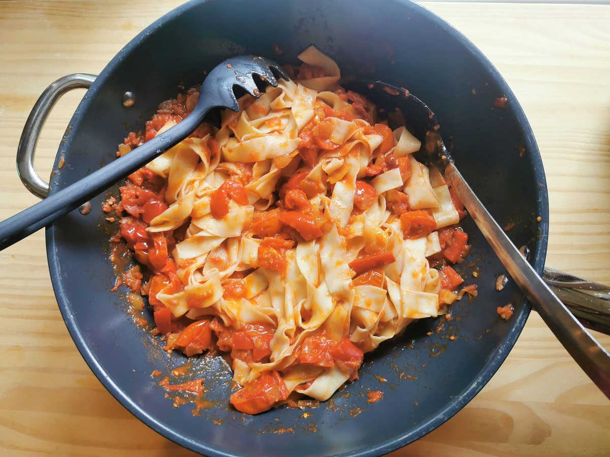 Cooked eggless tagliatelle mixed with tomato and sweet pepper sauce in large skillet