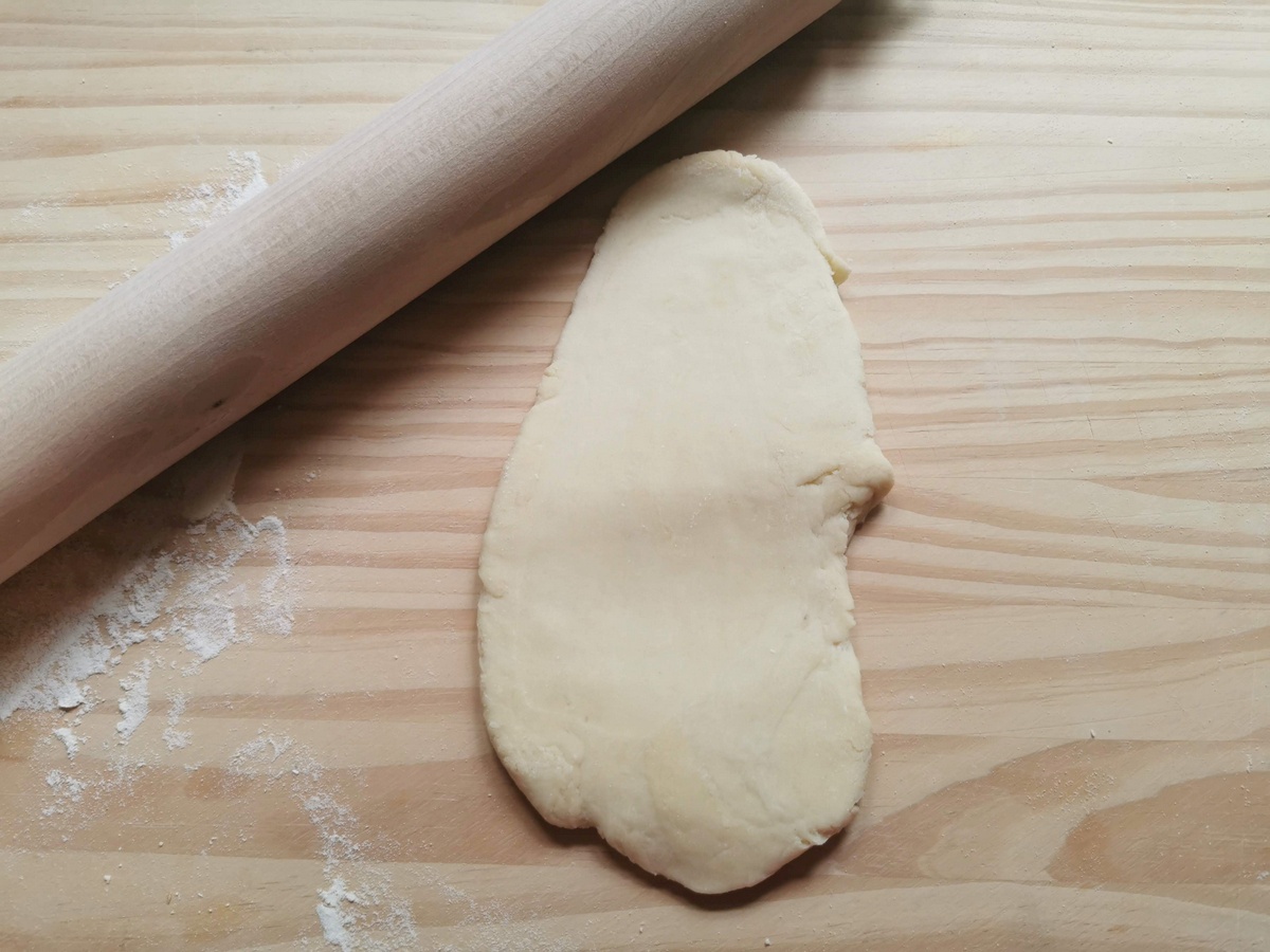 Piece of eggless tagliatelle dough rolled out with rolling pin on wood work top.