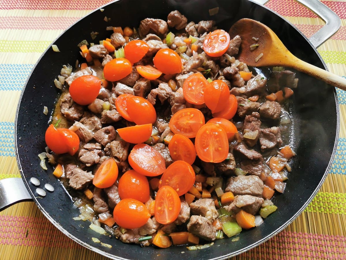 halved cherry tomatoes in skillet with lamb and vegetables