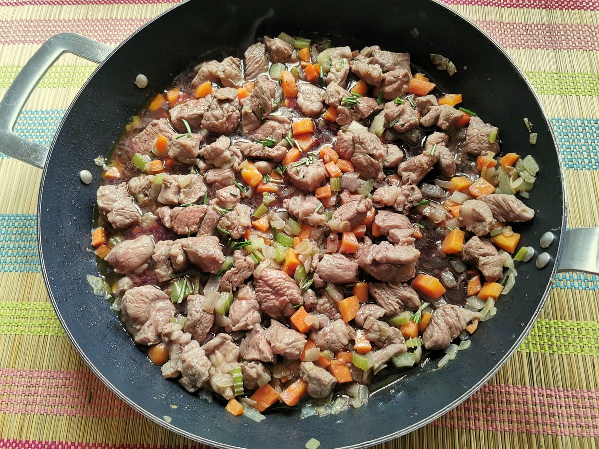 browned lamb with vegetables and herbs in skillet