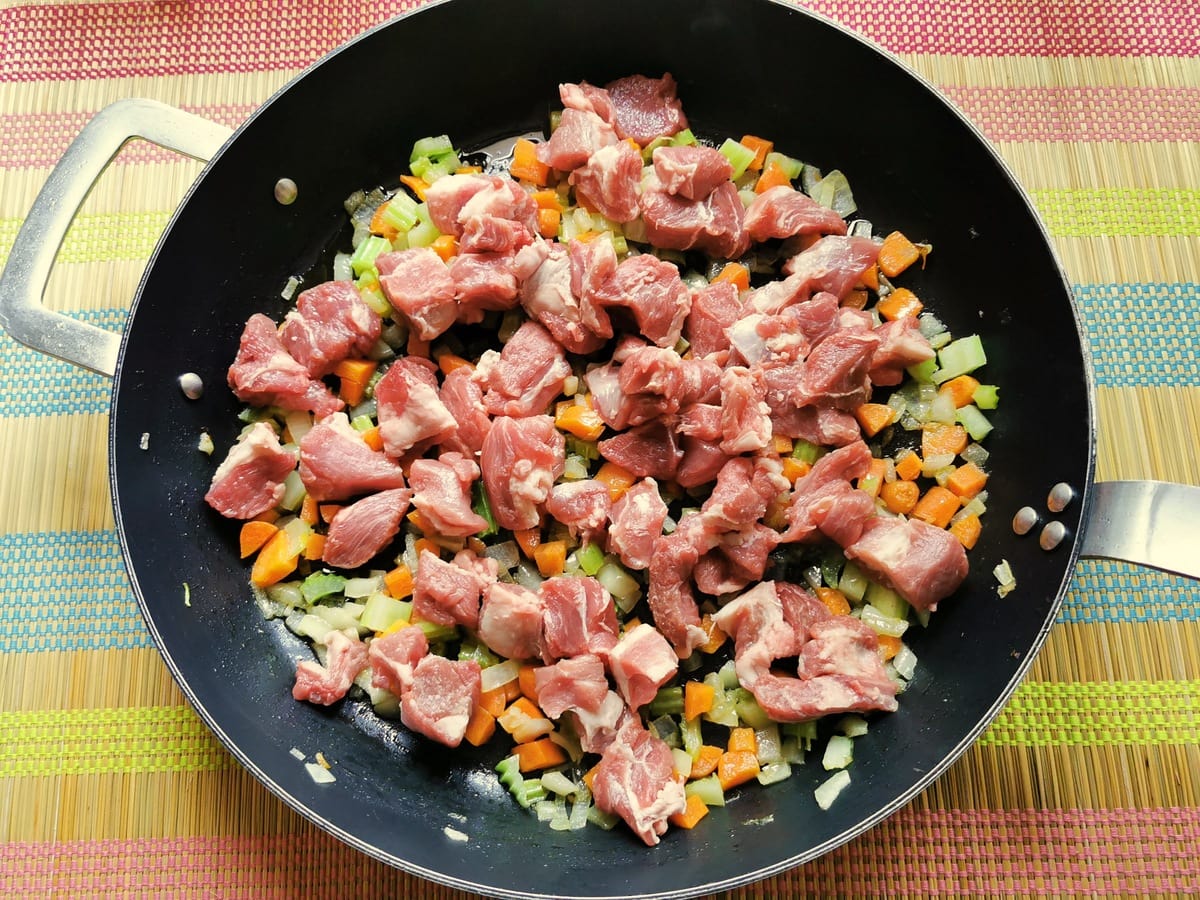 uncooked lamb pieces in skillet with onions, celery and carrots.