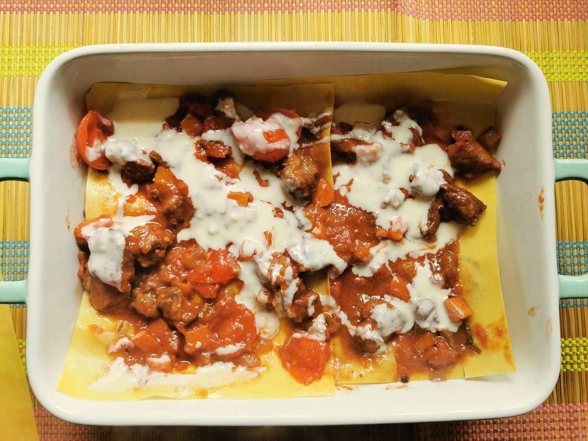 First layer of lasagne sheets with lamb ragu and béchamel on top in oven dish