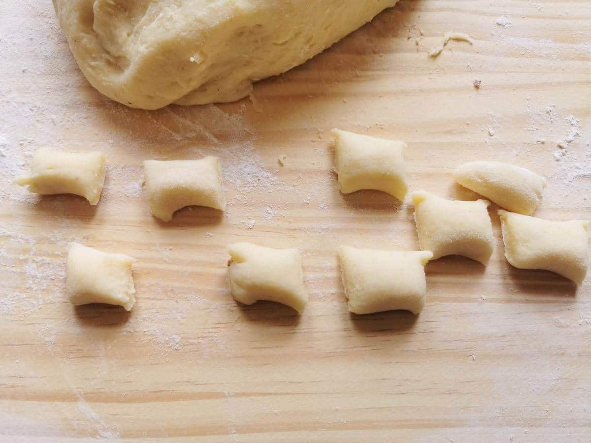 Gnocchi dough rope cut into pieces on wood work surface.
