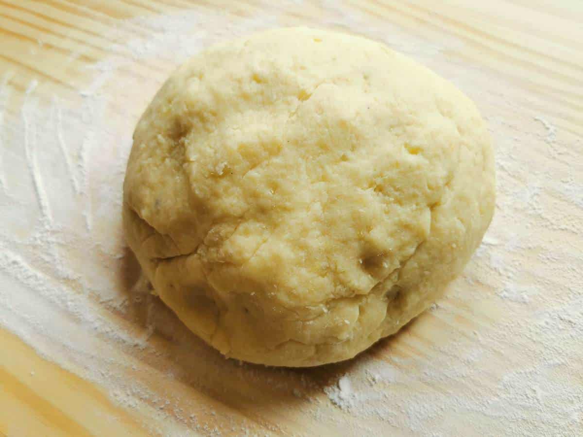 Ball of potato gnocchi dough on wood work surface dusted with flour.